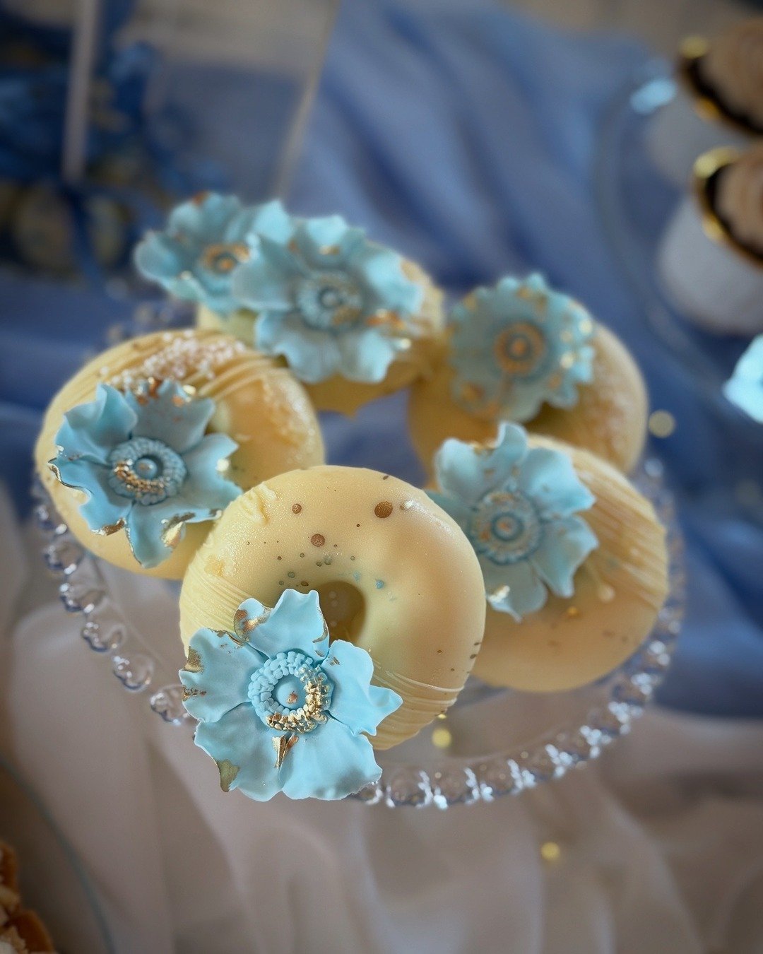 Donuty w białej czekoladzie udekorowane kwiatkiem - Pracownia Kremlove Małe donuty w białej czekoladzie i kwiatkiem w kolorze błekitu